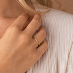 A hand wearing the gold Celeste Duo Marquise Ring with two small gemstones rests on pleated cream fabric.