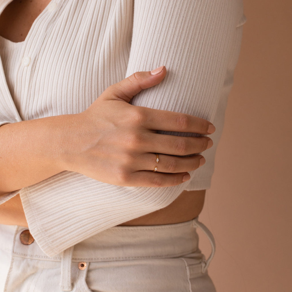 Wearing a ribbed cream top and light pants, the person gently holds their arm, showcasing the gold Celeste Duo Marquise Ring.