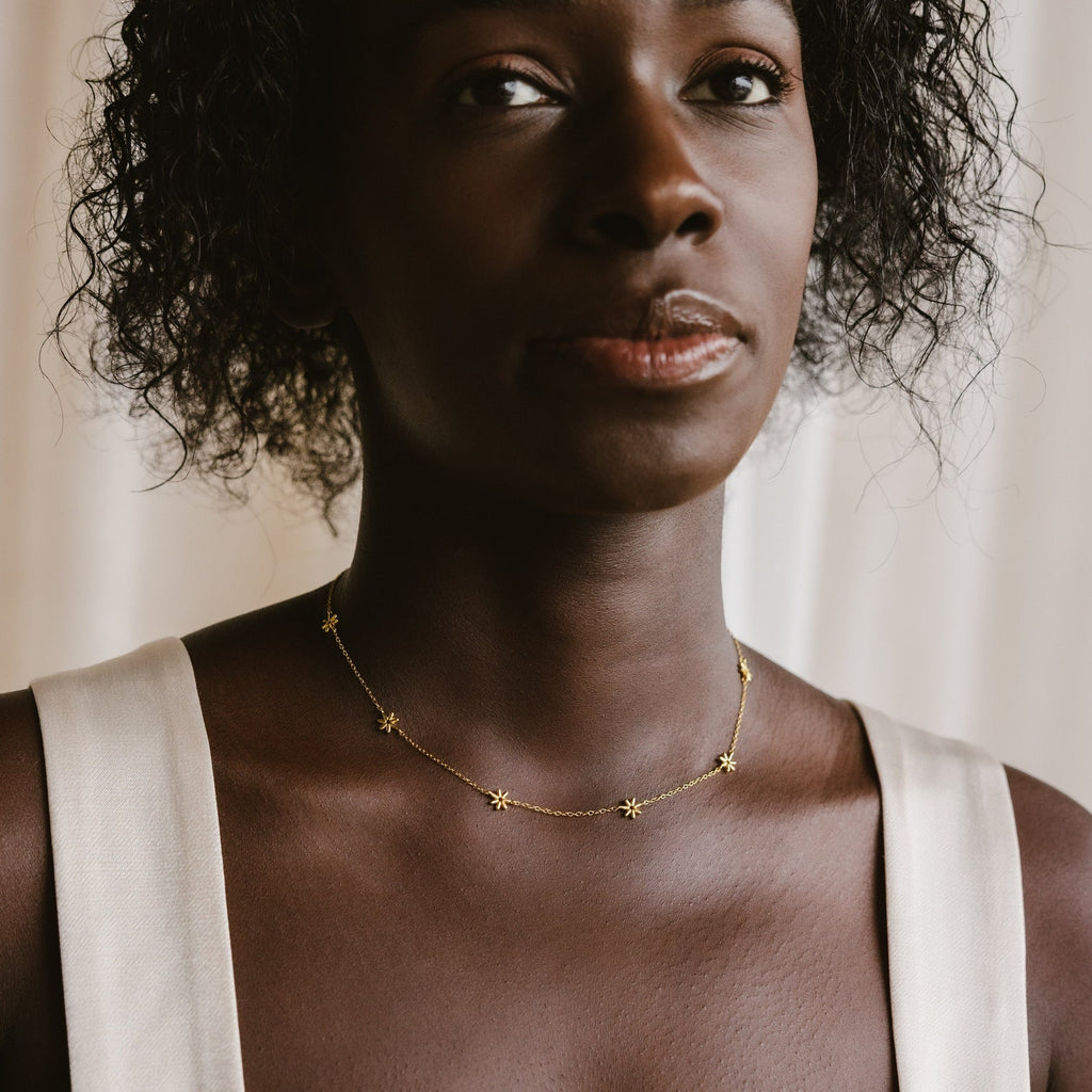 A woman wears a sleeveless white top paired with the Flower Child Necklace, adorned with delicate gold star-shaped charms—a perfect choice for bohemian jewelry lovers and effortless layering.