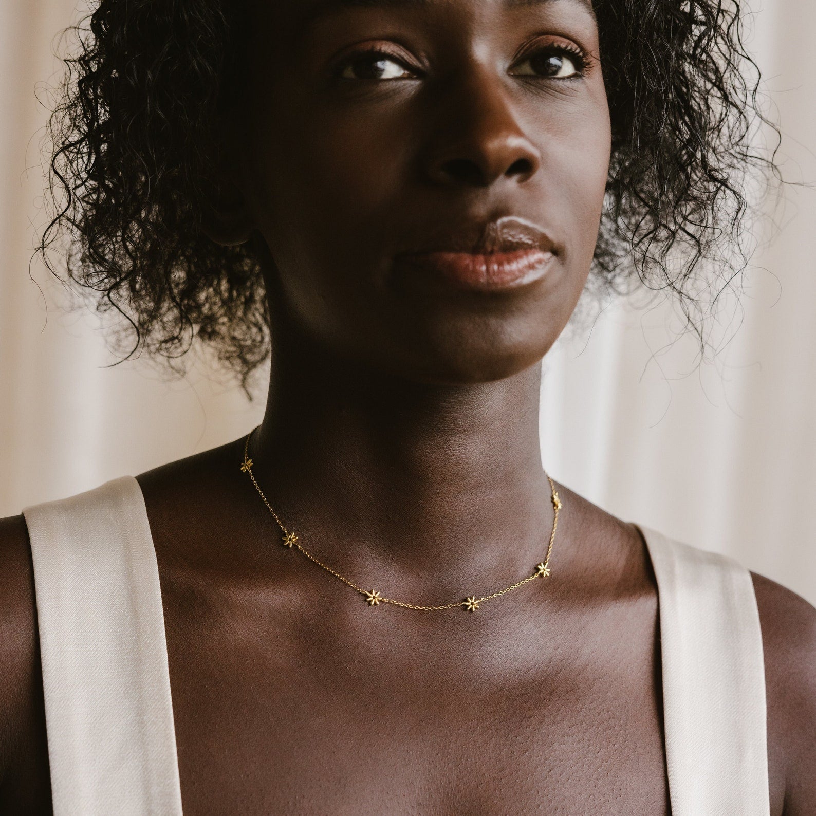A woman wears a sleeveless white top paired with the Flower Child Necklace, adorned with delicate gold star-shaped charms—a perfect choice for bohemian jewelry lovers and effortless layering.