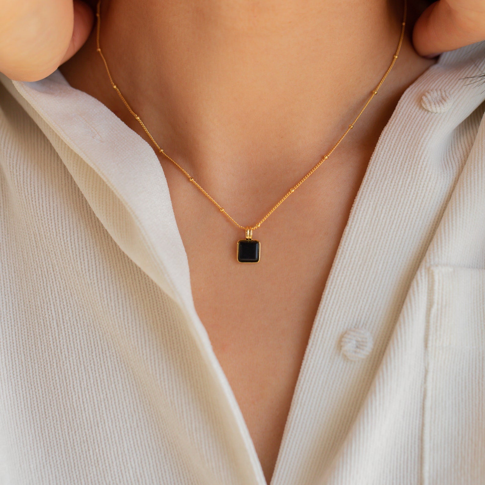 The Waverly Black Necklace features a gold satellite chain and bold black enamel pendant, perfect for layering over a crisp white collared shirt.