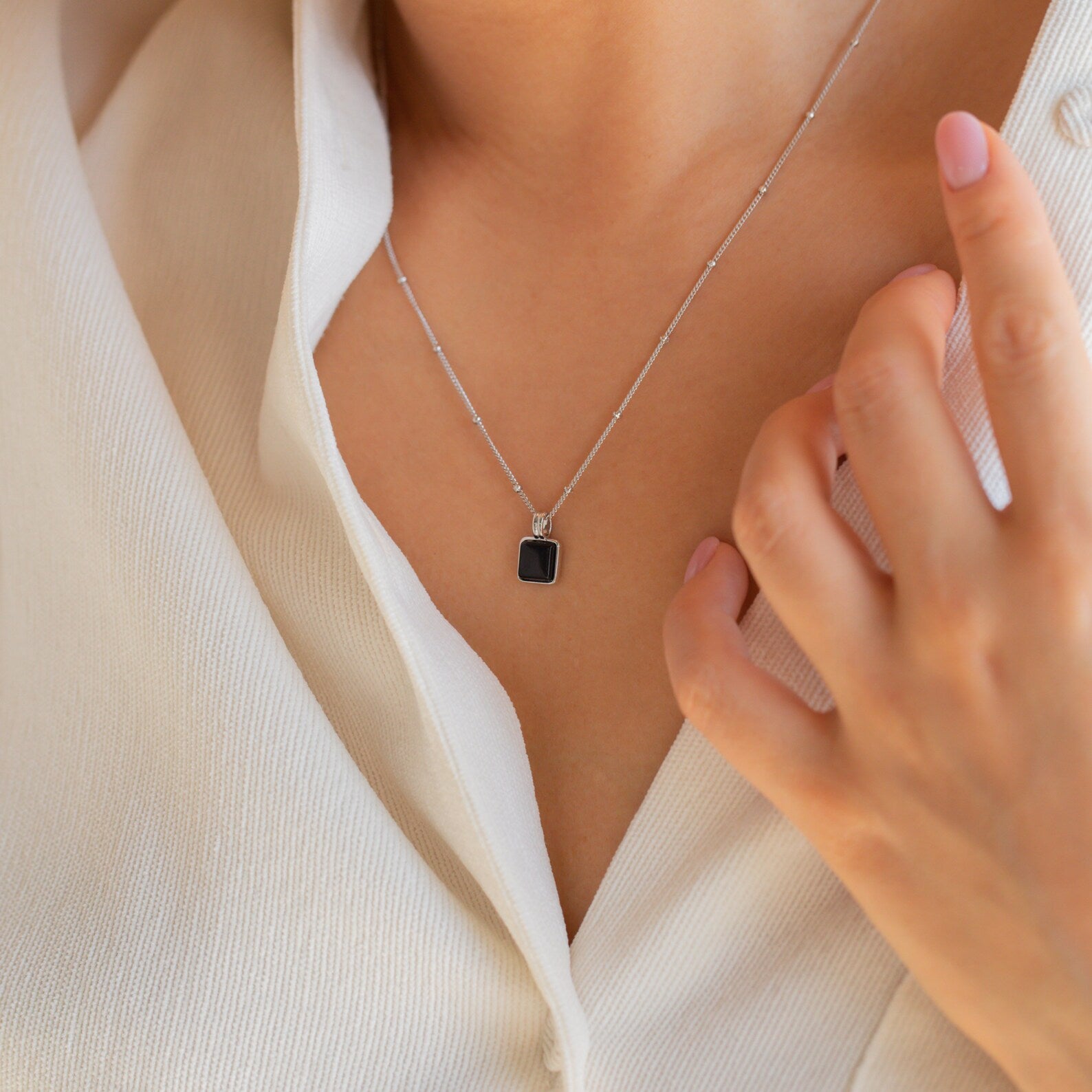 A person wearing the Waverly Black Necklace—a silver satellite chain with a black enamel pendant—dressed in a white shirt.