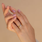 A hand with light pink nails wears the Mini Birthstone Ring and a gold band with small diamonds, set against a beige background.