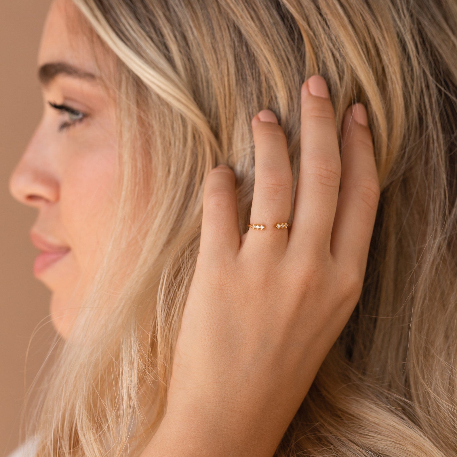 A woman touches her blonde hair, wearing the Serafina Diamond Ring—a delicate gold piece with small beads, perfect for those who love a dainty style.
