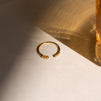 The Serafina Diamond Ring, a dainty gold piece with small clustered diamonds, rests on a sunlit surface and casts soft shadows.