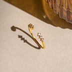 The Serafina Diamond Ring, a dainty gold open ring adorned with three small diamonds, casts a shadow on a light surface beside a textured glass object.