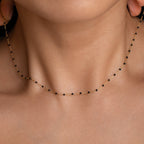 Close-up of a woman wearing the Black Station Necklace—a delicate black and gold beaded piece that highlights an elegant fashion trend against bare skin.
