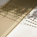 The Black Station Necklace, a beaded fashion accessory, is displayed diagonally on a beige and cream background with soft shadows.