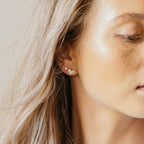 Close-up of a woman with blonde hair wearing Trixie Diamond Studs—small, gold, heart-shaped earrings on her left ear that reflect the subtle elegance of modern classic jewelry.
