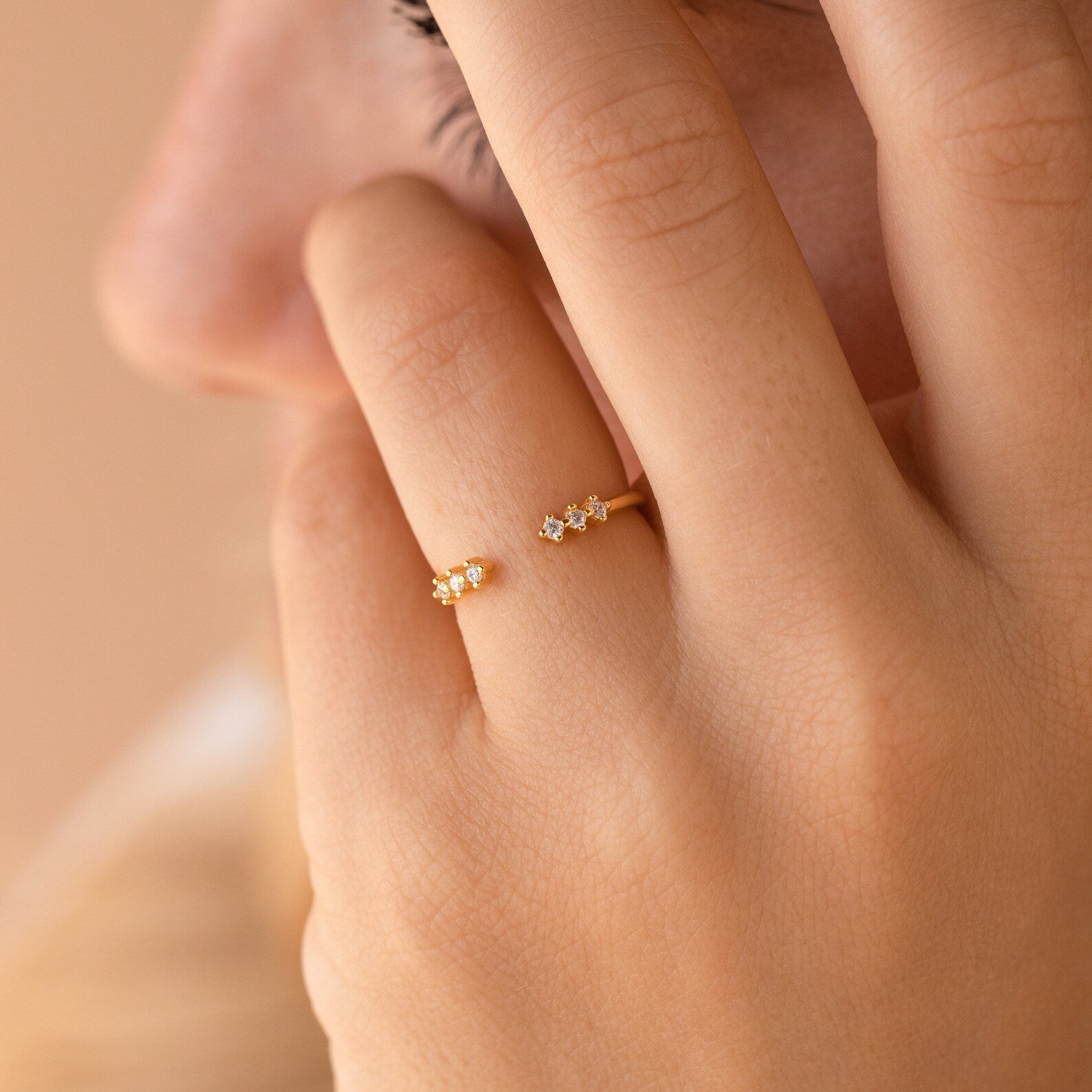 A hand adorned with the Serafina Diamond Ring, featuring a delicate and dainty floral design in gold, posed gently near the lips and cheek.