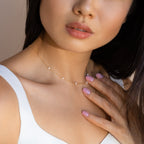 Woman wearing the Opal Station Necklace, a delicate minimalist piece featuring small opals, touches her neck while sporting light pink nail polish.