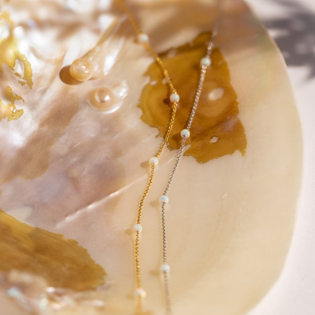 The Opal Station Necklace, featuring delicate opal stones in a minimalist design, is displayed on an iridescent seashell.