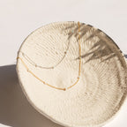 Gold and silver chain necklaces with evenly spaced small opal beads, displayed draped inside a textured cream ceramic bowl.