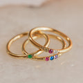 The Mini Birthstone Ring features a slim gold band set with vibrant gemstones, shown on a light marble surface—a delicate, elegant choice for everyday wear or as a personalized birthstone ring.