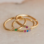 The Mini Birthstone Ring features a slim gold band set with vibrant gemstones, shown on a light marble surface—a delicate, elegant choice for everyday wear or as a personalized birthstone ring.