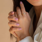 Close-up of hands with light pink nail polish wearing the Mini Birthstone Ring and a gold band, set against a neutral background.