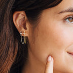 A woman smiles, touching her cheek while wearing Florence Diamond Chain Earrings; a close-up highlights the sparkling crystal accents and elegant double chain design.