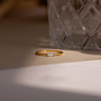 The Eloise Opal Ring, featuring a small iridescent stone, rests beside textured glass in soft lighting, capturing the essence of minimalism.