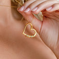 A person holds a Custom Bead Heart Necklace—a gold heart pendant with personalized engraved beads on a delicate chain.