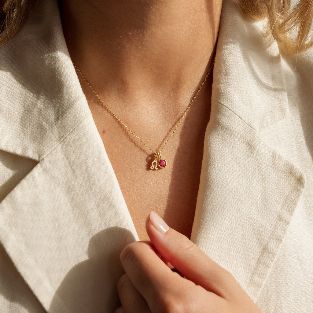 Woman wearing a cream blazer and the Zodiac Birthstone Necklace featuring a small gold pendant with a pink gemstone, adding a personalized jewelry touch.