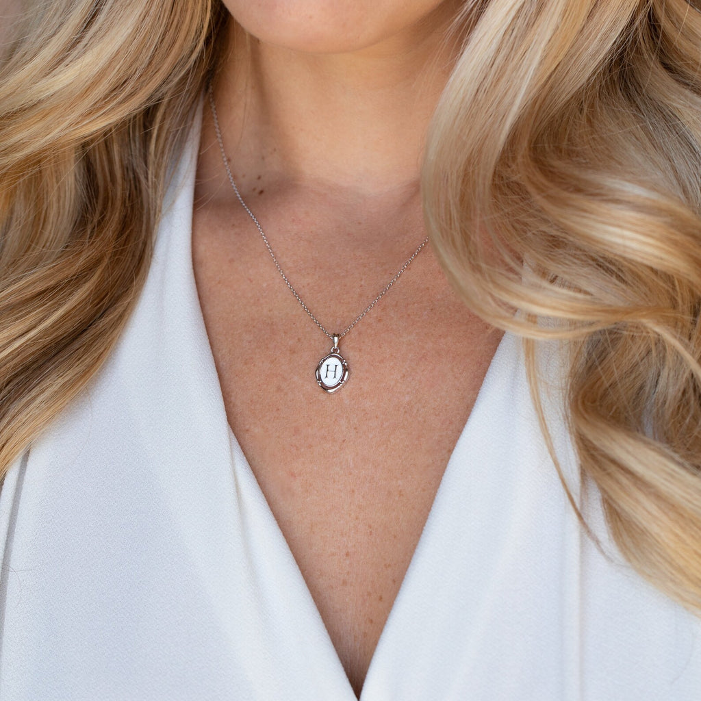 Woman with long blonde hair wears a white top and the Initial Pendant Necklace in Sterling Silver, featuring a vintage-inspired silver oval pendant.