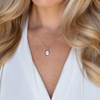 Woman with long blonde hair wears a white top and the Initial Pendant Necklace in Sterling Silver, featuring a vintage-inspired silver oval pendant.