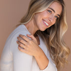A woman smiles with her hand on her shoulder, displaying the elegant Mariposa Diamond Ring.