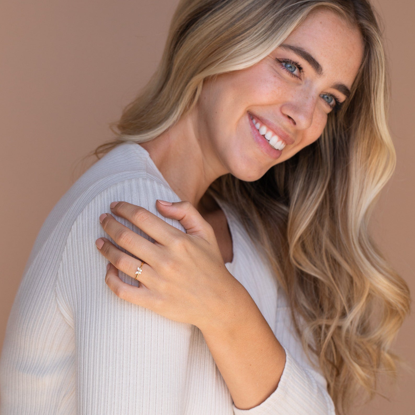 A woman smiles with her hand on her shoulder, displaying the elegant Mariposa Diamond Ring.