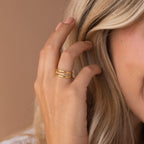 A blonde woman wears three stacked gold rings, including the Amani Pave Twist Ring, on her hand near her face.