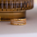 The Amani Pave Twist Ring features multiple intertwined gold bands, some adorned with sparkling CZ diamonds, displayed on a light surface.