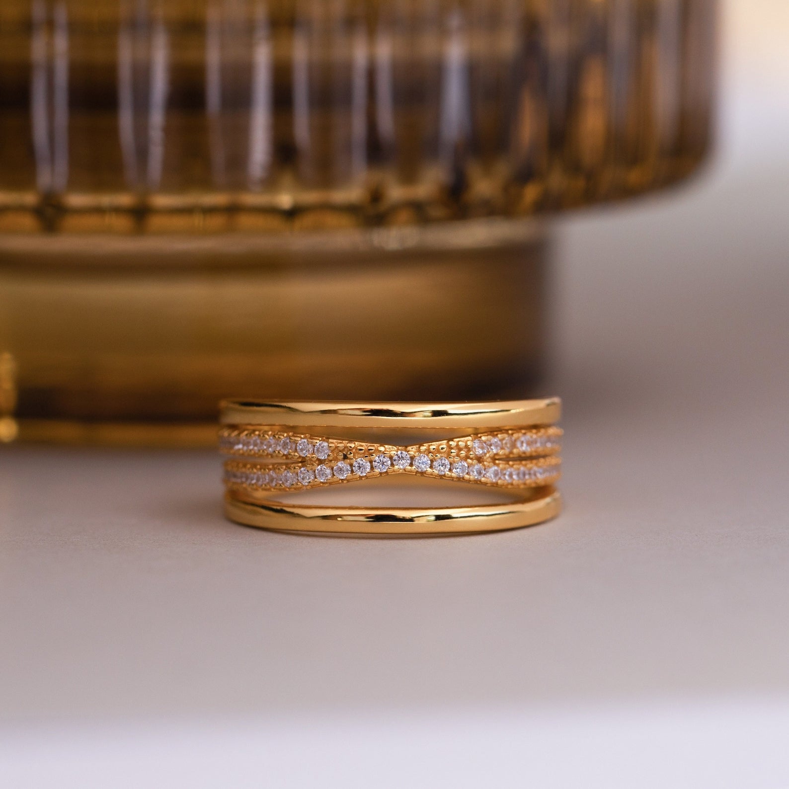 The Amani Pave Twist Ring features multiple intertwined gold bands, some adorned with sparkling CZ diamonds, displayed on a light surface.