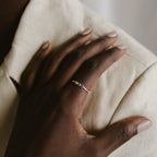 A hand with neatly manicured nails rests on a shoulder, highlighting the Tiny Triple Birthstone Ring—its thin band and trio of tiny gemstones offer a touch of subtle elegance.