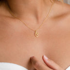 A woman wearing the Letter Heart Necklace—a minimalist gold heart pendant—holds her hand near her collarbone.