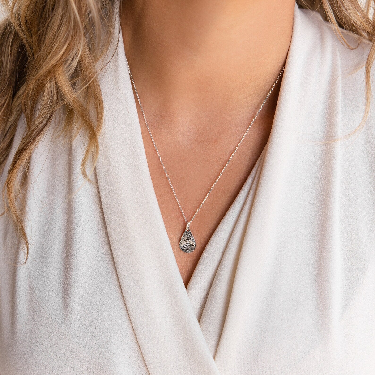 A woman wearing the Tear Drop Fingerprint Necklace with a white V-neck blouse.