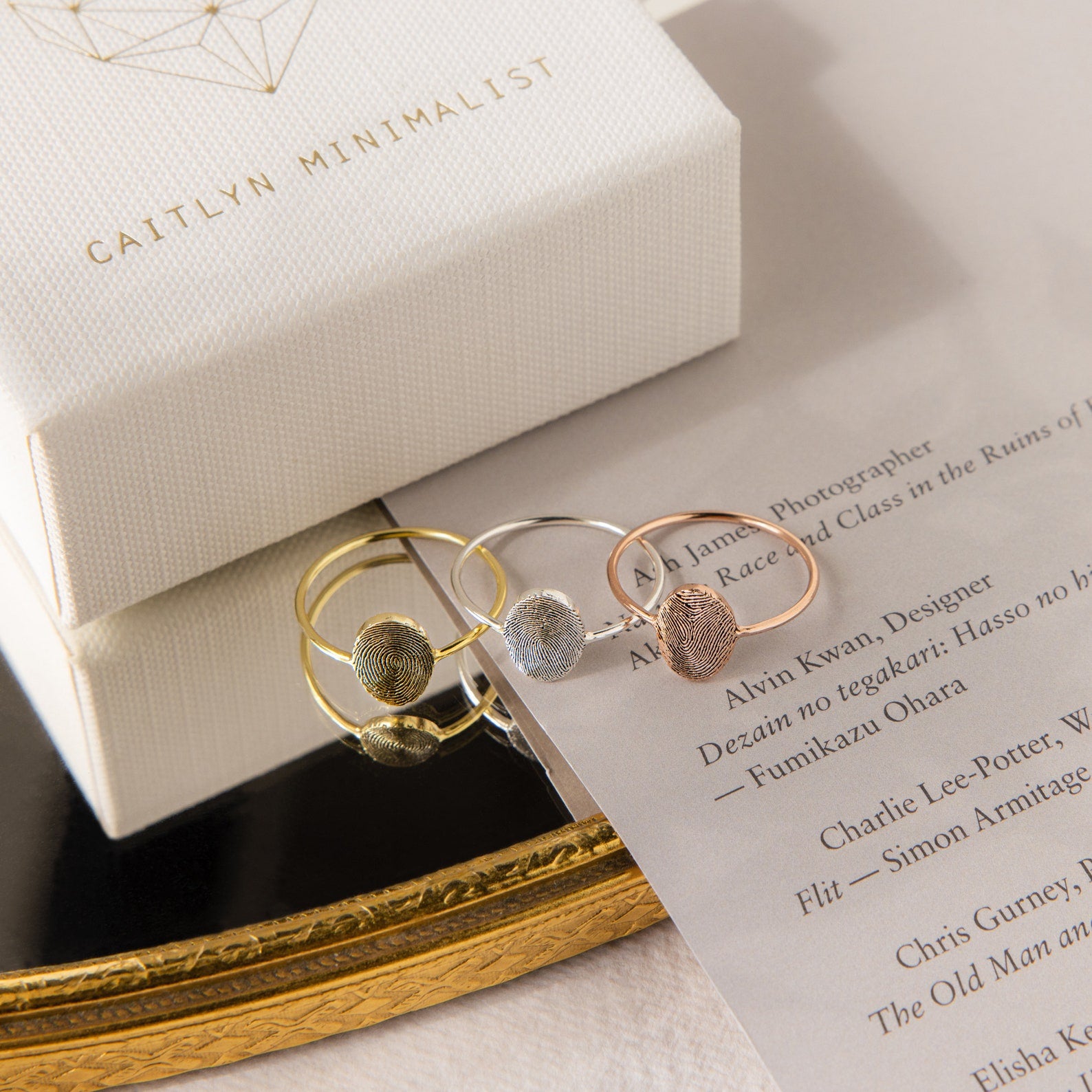 The Fingerprint Oval Ring, a handcrafted minimalist piece in gold, silver, and rose gold, is displayed on a card beside a branded jewelry box.