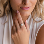A woman touches her face while wearing the Fingerprint Oval Ring, a handcrafted silver accessory with an oval white stone, paired with a sleeveless white top.