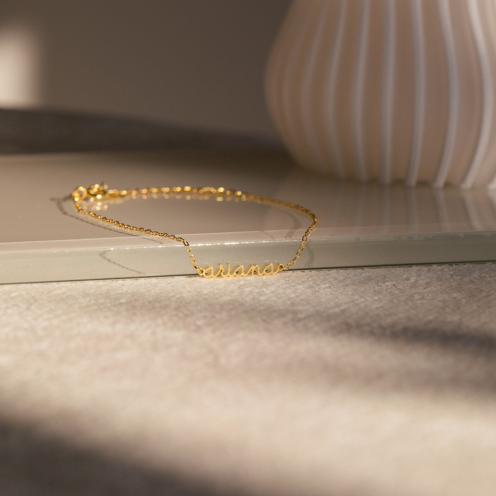 The Dainty Tiny Name Bracelet rests on a beige surface in soft natural light—ideal for fans of minimal jewelry and personalized gifts who love delicate, custom accessories.