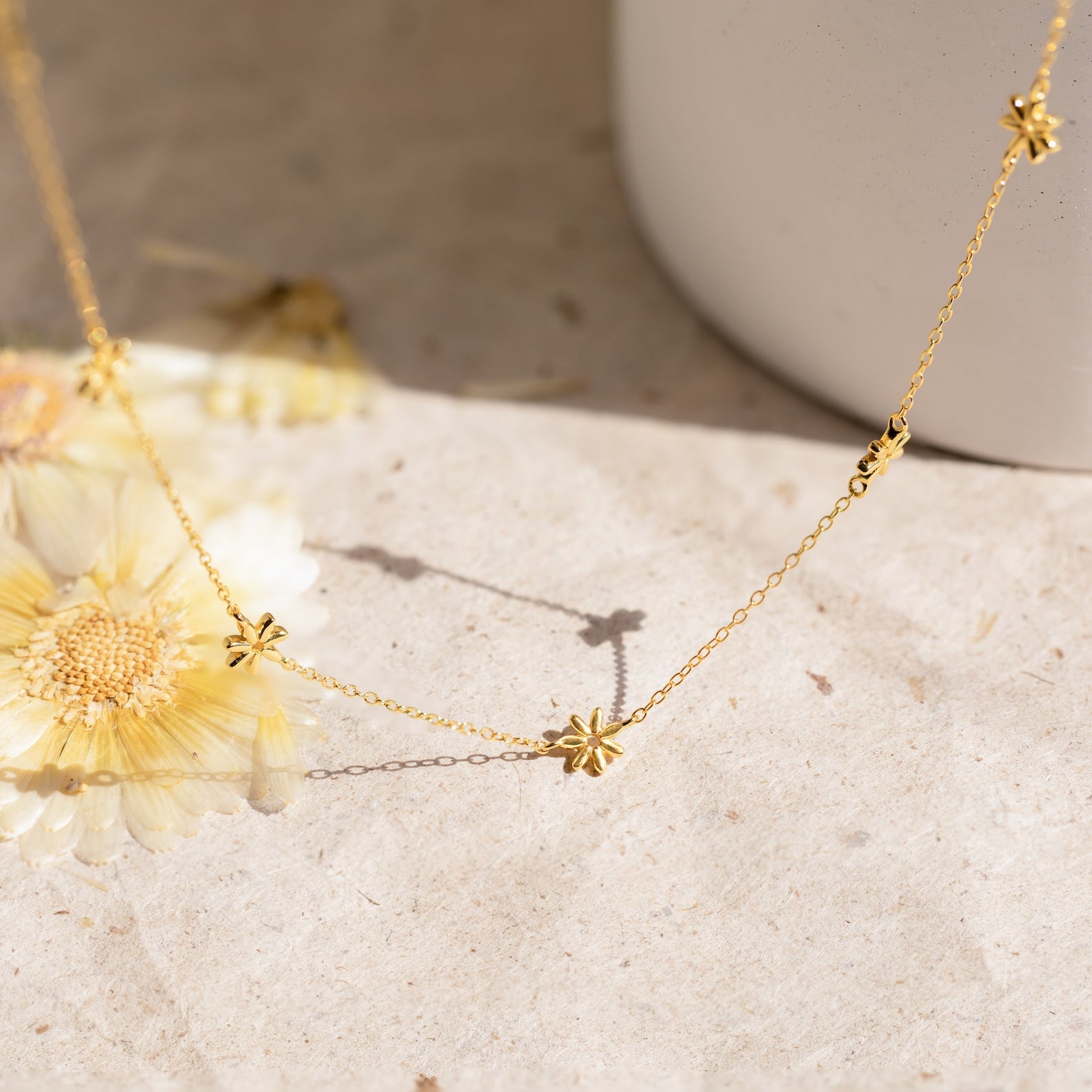 The Flower Child Necklace features small star-shaped charms, perfect for bohemian jewelry lovers. Shown near dried flowers and a white vase, it's an ideal delicate layering piece.