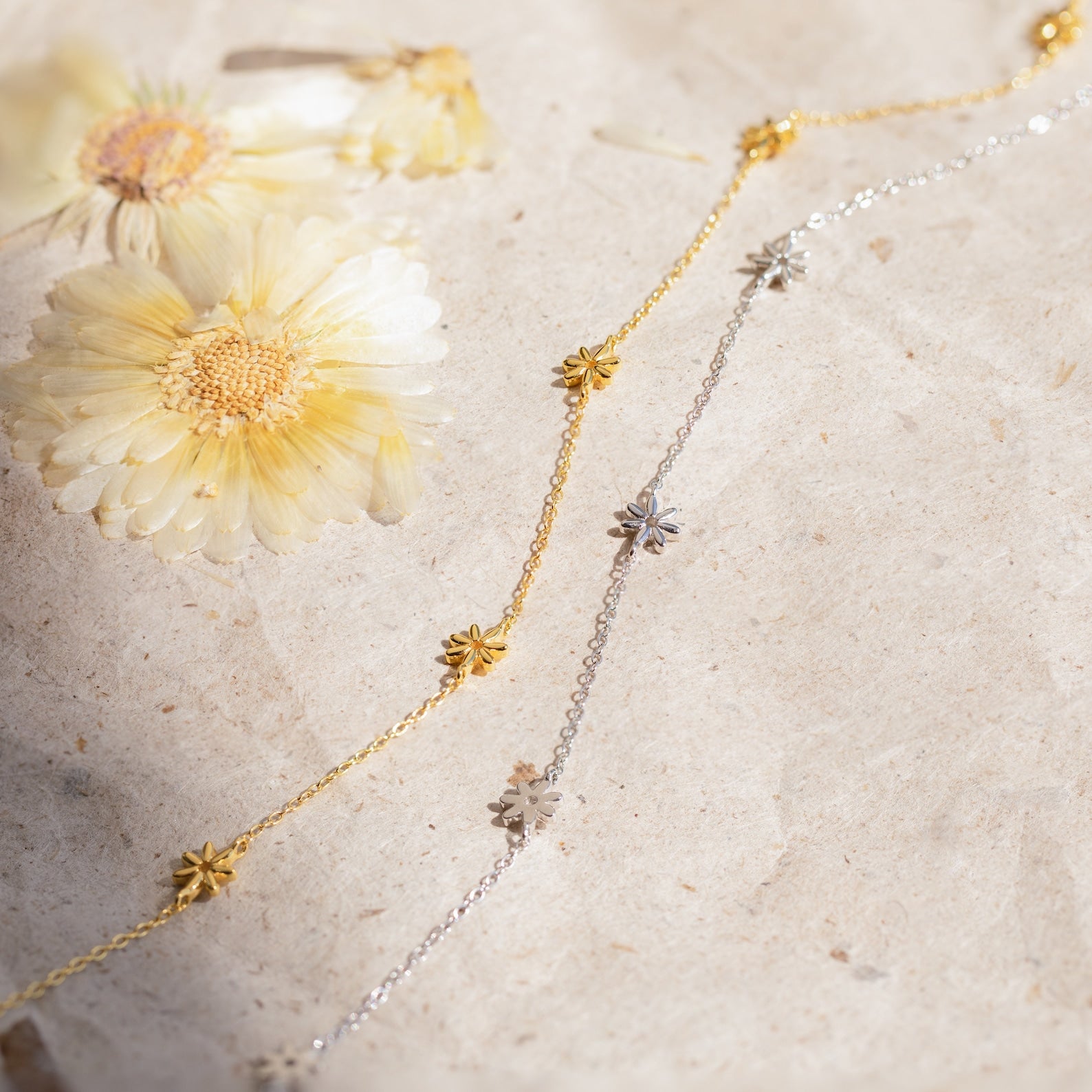 The Flower Child Necklace, ideal for layering with gold and silver daisy chains, is displayed on a textured surface with dried flowers—a dreamy bohemian jewelry piece.