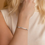 A woman wears the Custom Message Cuff, a silver engraved bracelet with "I AM ENOUGH" on her wrist—an inspiring personalized gift.