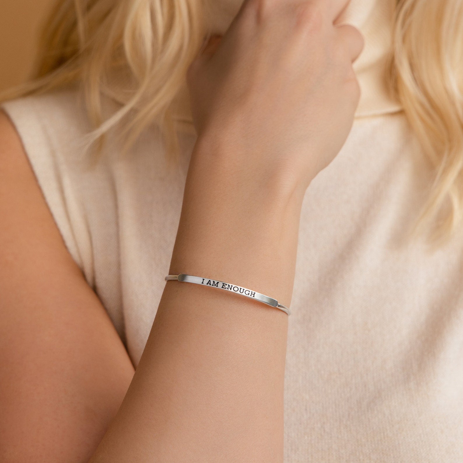 A woman wears the Custom Message Cuff, a silver engraved bracelet with "I AM ENOUGH" on her wrist—an inspiring personalized gift.