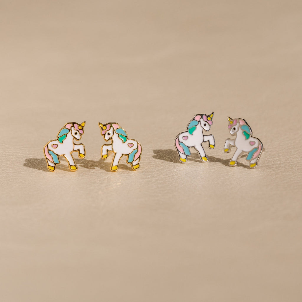 Unicorn Studs: Four pastel enamel unicorn earrings with gold edges on a beige surface—an adorable gift for girls who love whimsical jewelry.