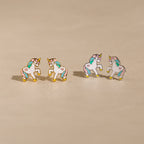 Unicorn Studs: Four pastel enamel unicorn earrings with gold edges on a beige surface—an adorable gift for girls who love whimsical jewelry.
