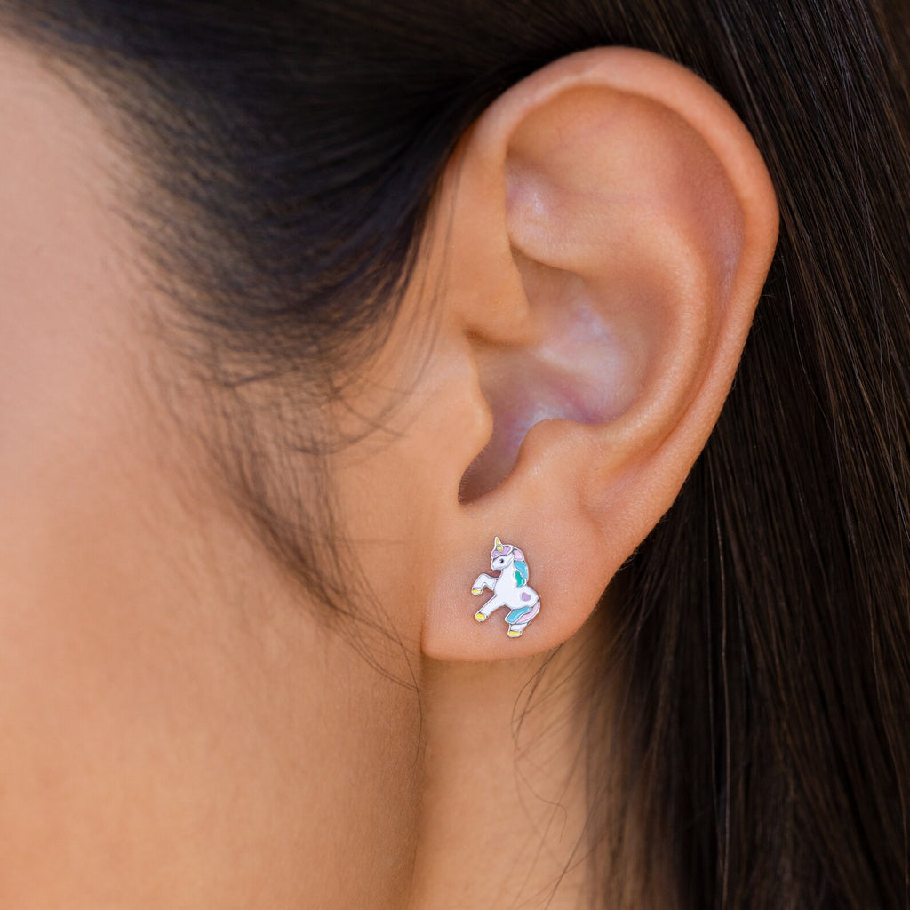 A close-up of an ear wearing Unicorn Studs—small, pastel enamel unicorn earrings that are a charming and colorful gift for girls.