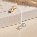 Two pairs of Unicorn Studs—small, colorful pastel enamel earrings—are displayed on a textured surface and white jewelry box, making a delightful gift for girls.