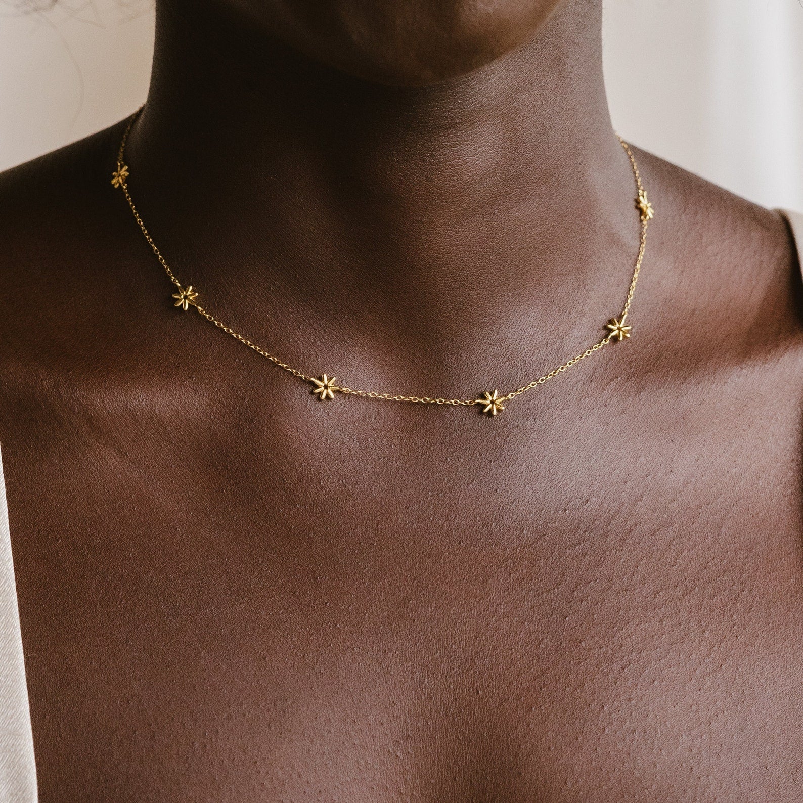 Close-up of the Flower Child Necklace, a gold layering necklace with small star charms on a person’s neck—perfect for adding bohemian jewelry vibes.