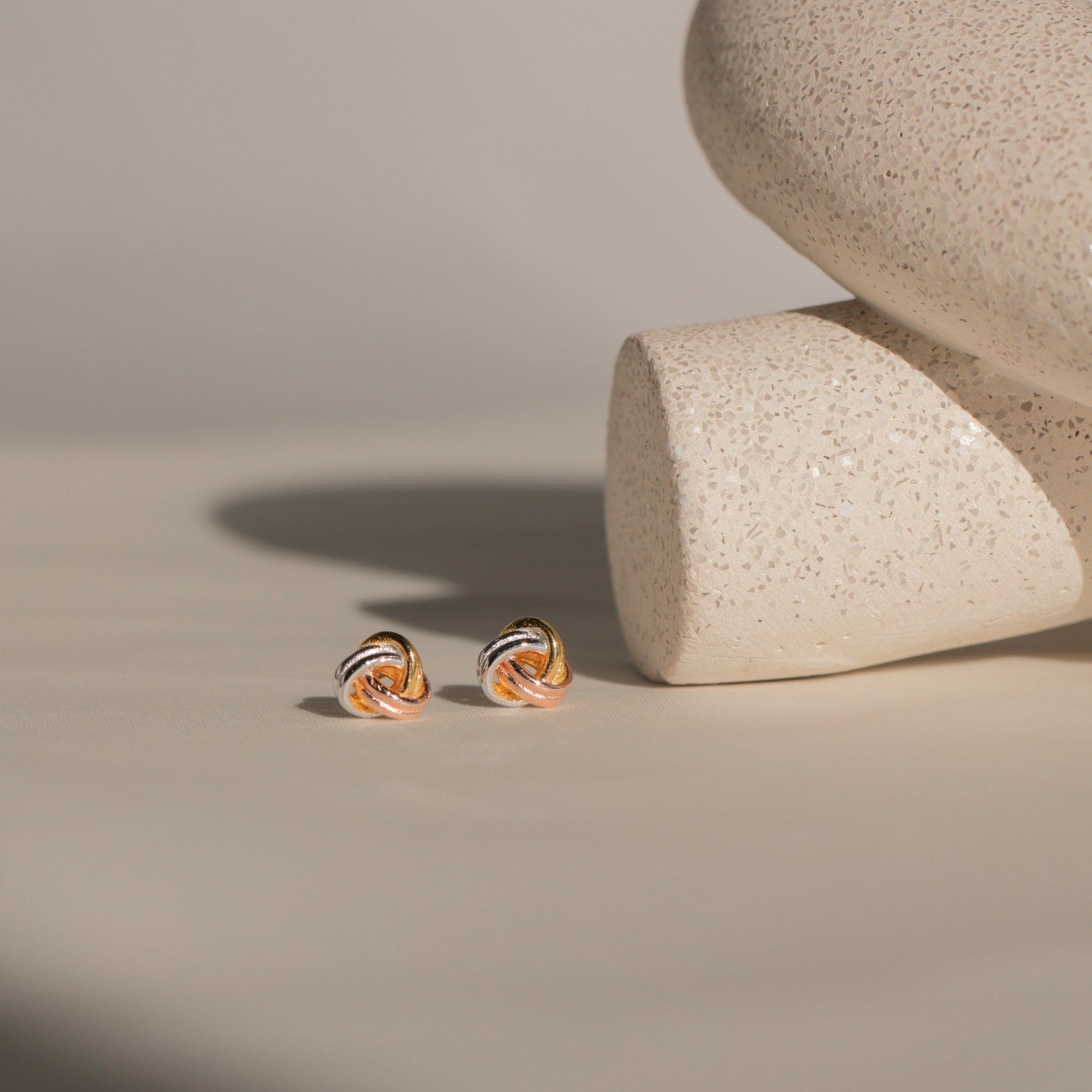 Trinity Knot Studs displayed on a light beige surface with textured ceramic accents—an ideal, thoughtful anniversary gift.