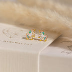 Unicorn Studs—small, colorful earrings—are displayed on a textured white surface next to soft beige faux fur, making them a charming gift for girls.