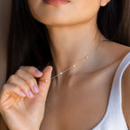 A woman with long dark hair wears a white tank top and holds the delicate handmade Opal Station Necklace near her neck, highlighting the minimalist elegance of this unique piece.