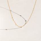 Delicate gold chain necklace with evenly spaced small opal beads, shown casting soft shadows on a light cream background.